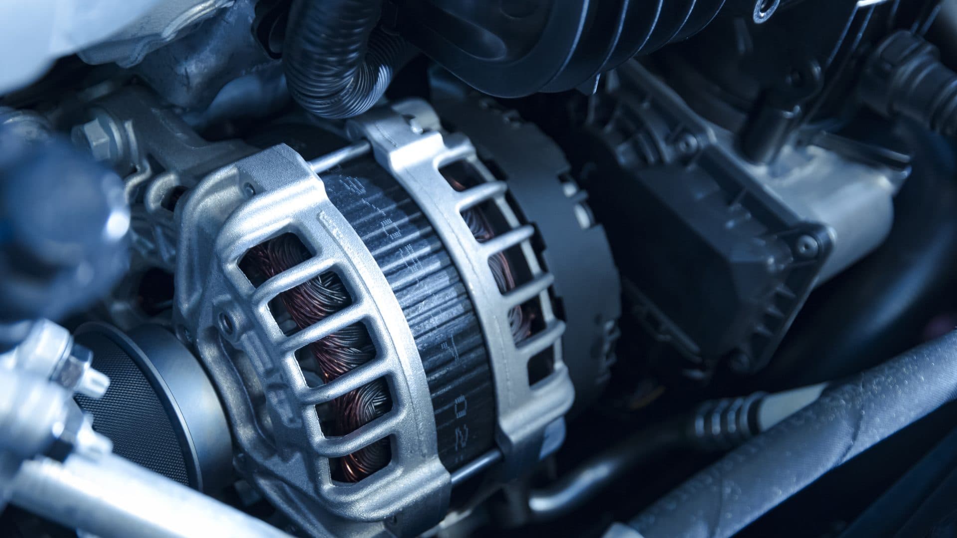 Open hood of a white car in a dark garage showing the battery and alternator